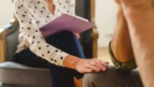 A woman placing her hand on the knee of a men while consulting him