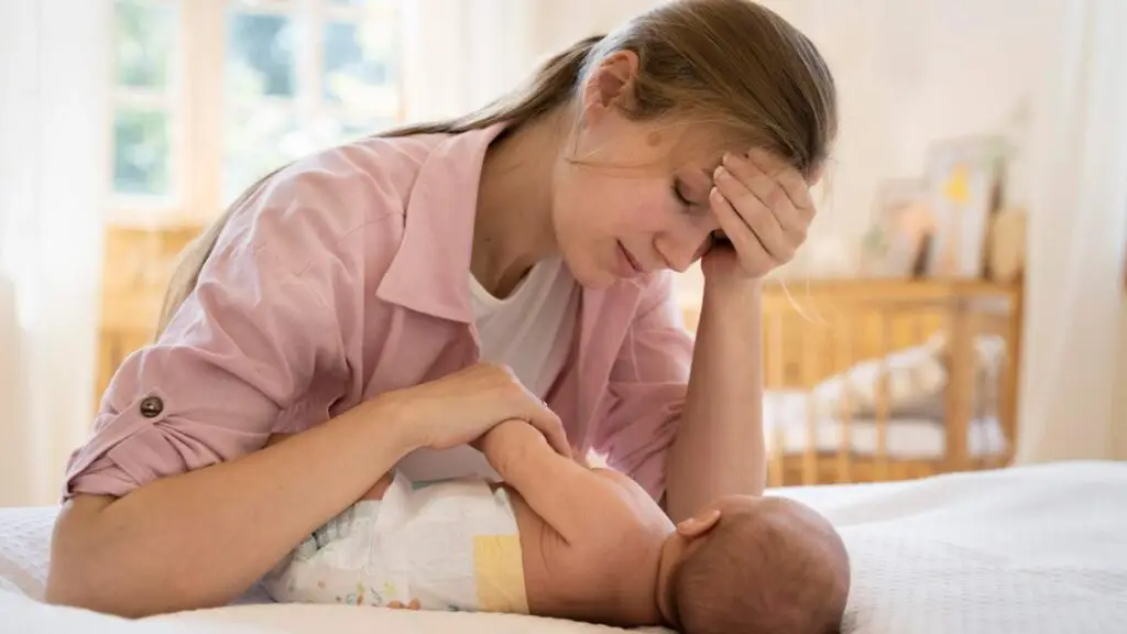 Exhausted mother with baby on bed at home